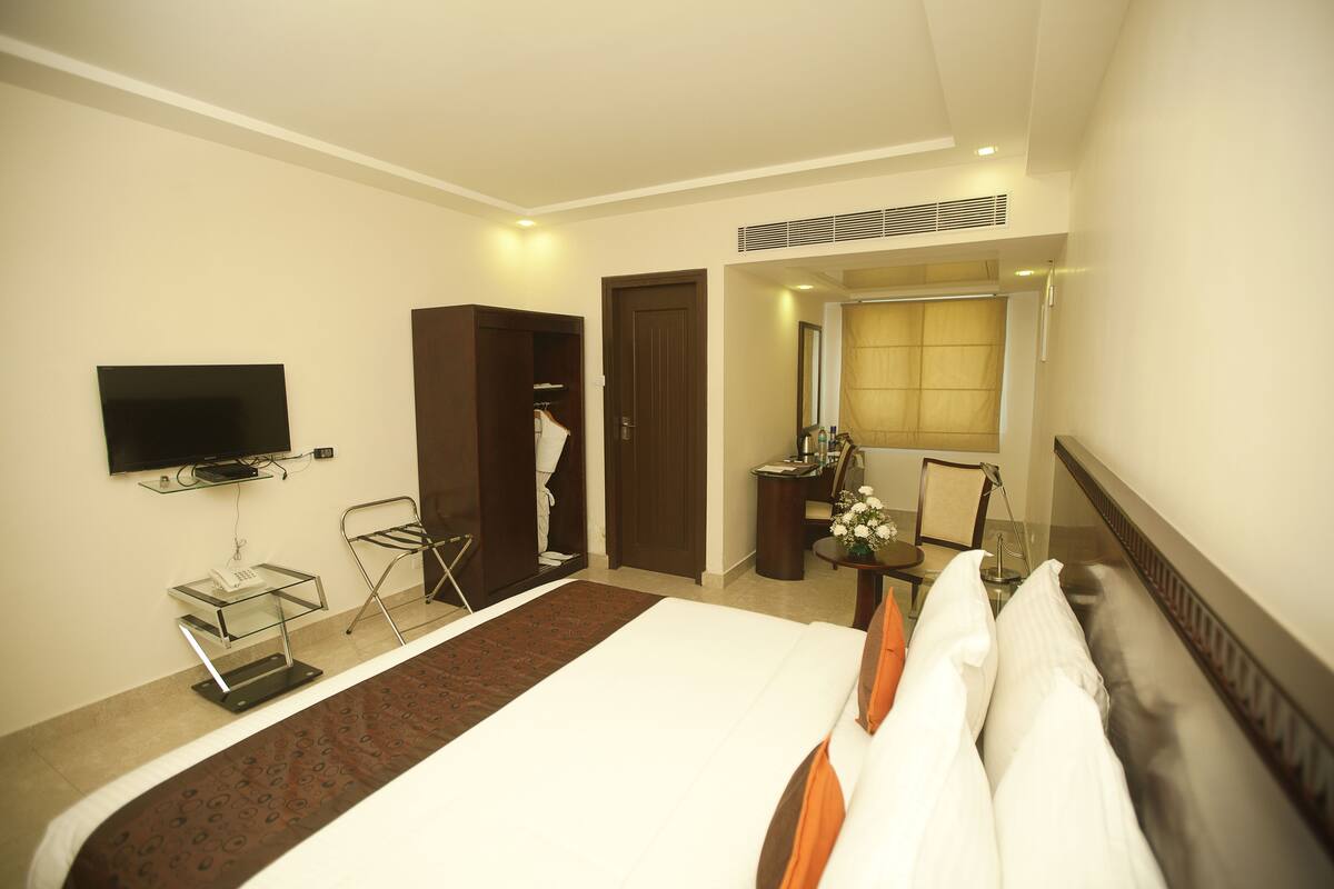 A hotel room with a bed, a television mounted on the wall, a wardrobe, a mirror, and a desk with a chair.
