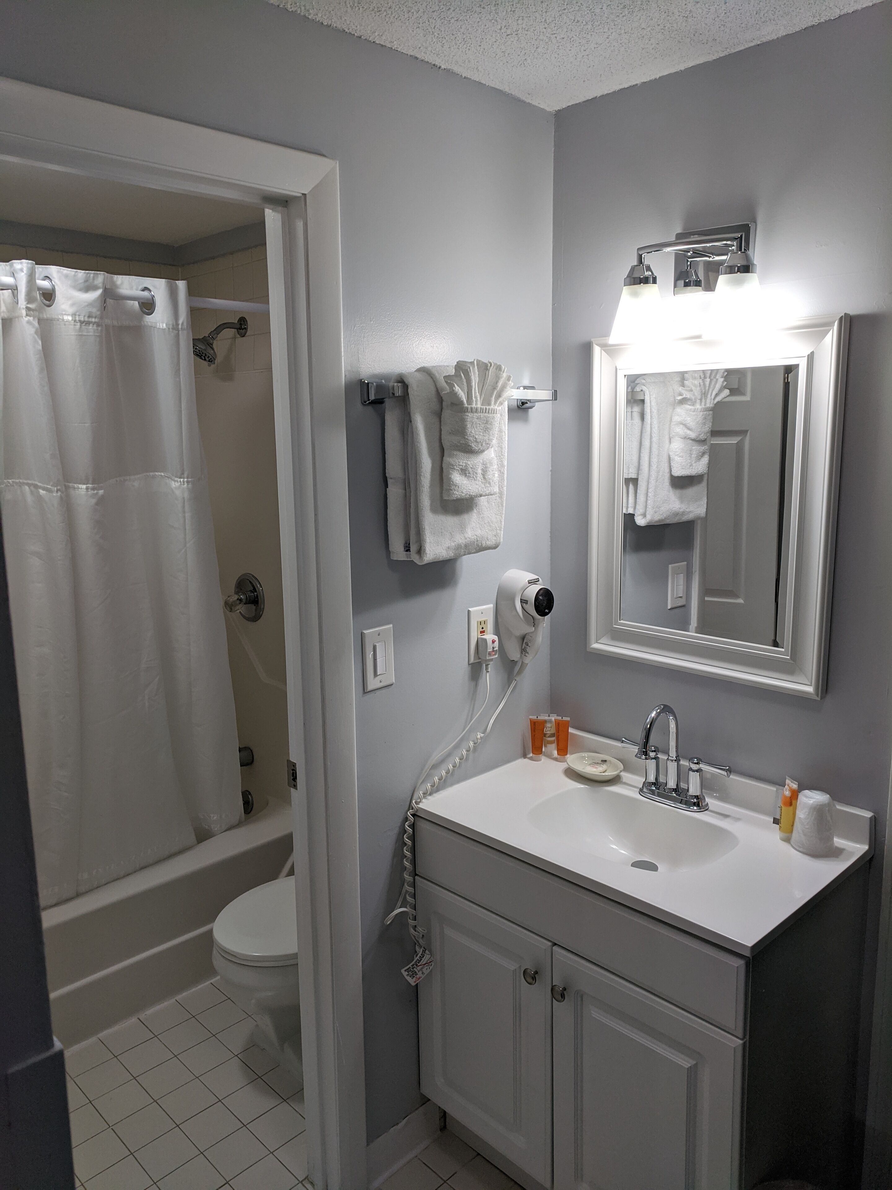 A bathroom with a shower, toilet, sink, and a mirror.