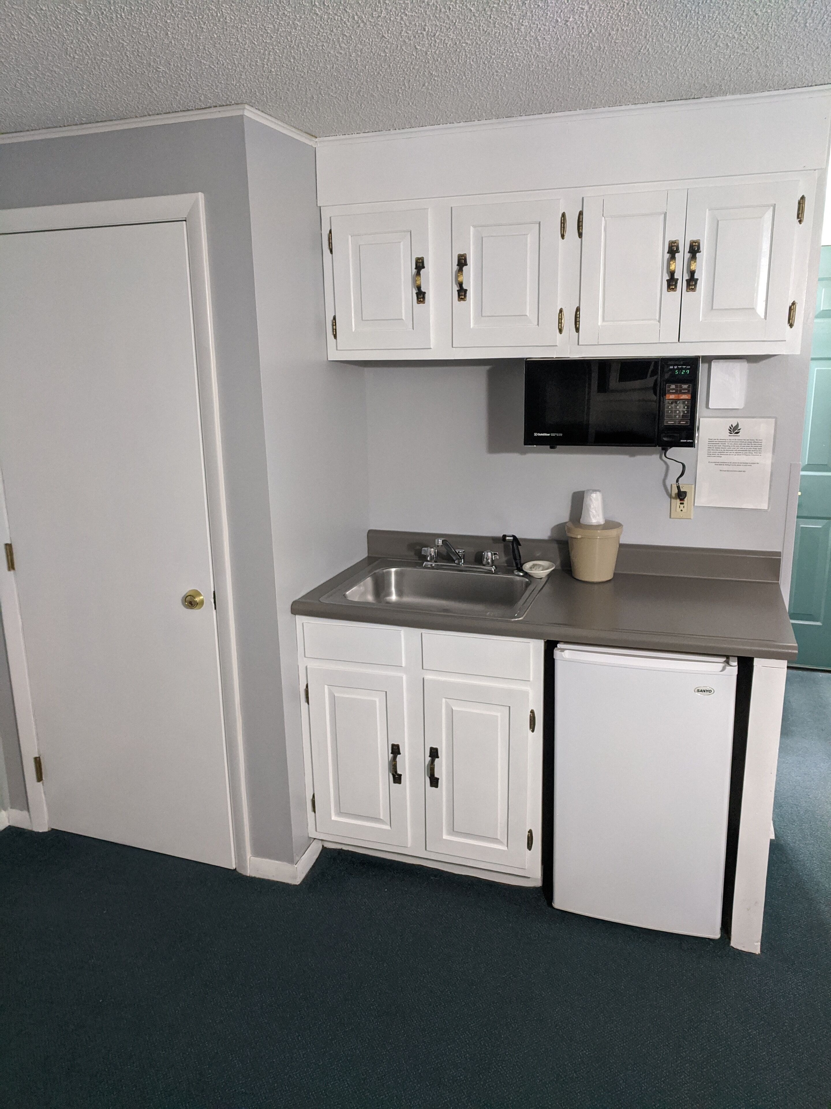 Een kleine keuken met witte kastjes, een magnetron en een spoelbak.