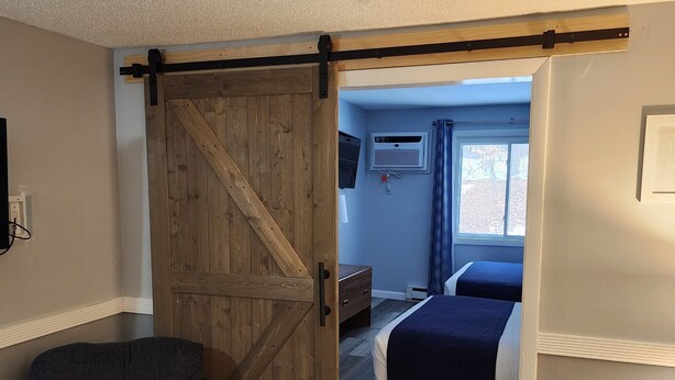 A room with a wooden sliding door leading to a bedroom with a bed and a window. - Eastern Inn & Suites (North Conway)