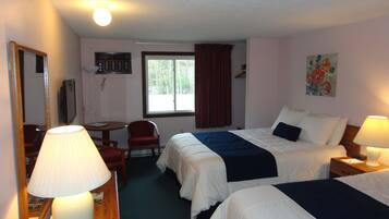 A hotel room with two beds, a desk, a chair, a lamp, a painting, and a window with curtains.