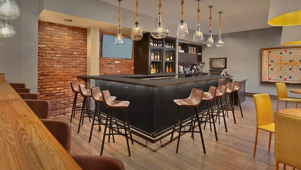 Een moderne bar met een centraal bar eiland, barstoelen, hangende verlichtingsarmaturen, een metselwerk accentmuur en een televisie.