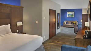 Een hotelkamer met een groot bed, een bureau met stoel, een bank en een schilderij aan de muur.