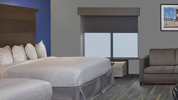 Habitación de hotel con una cama grande, una cama más pequeña, un sillón gris, una ventana con persianas y un cuadro en la pared.