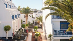 Een binnenplaats met een zwembad, palmbomen en een trap die naar een gebouw met een blauw balkon leidt.