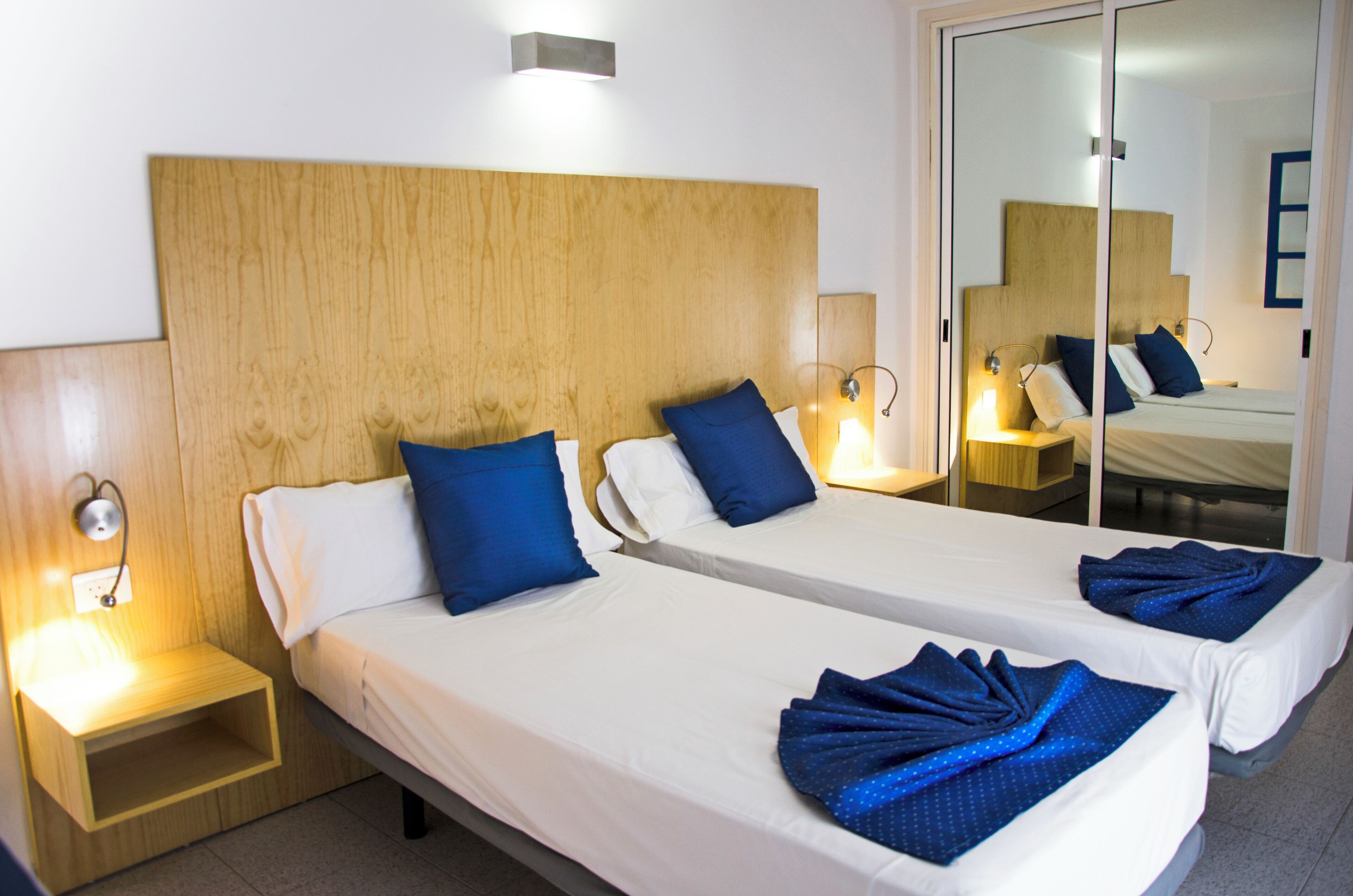 A hotel room with two single beds, wooden headboard, bedside lamps, and a mirror.