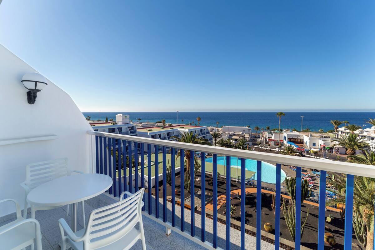 A balcony with a pool view, white chairs, and a clear blue sky.