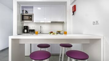 A modern kitchen with white cabinets, a microwave, a coffee maker, and a sink. There are purple stools at the counter.