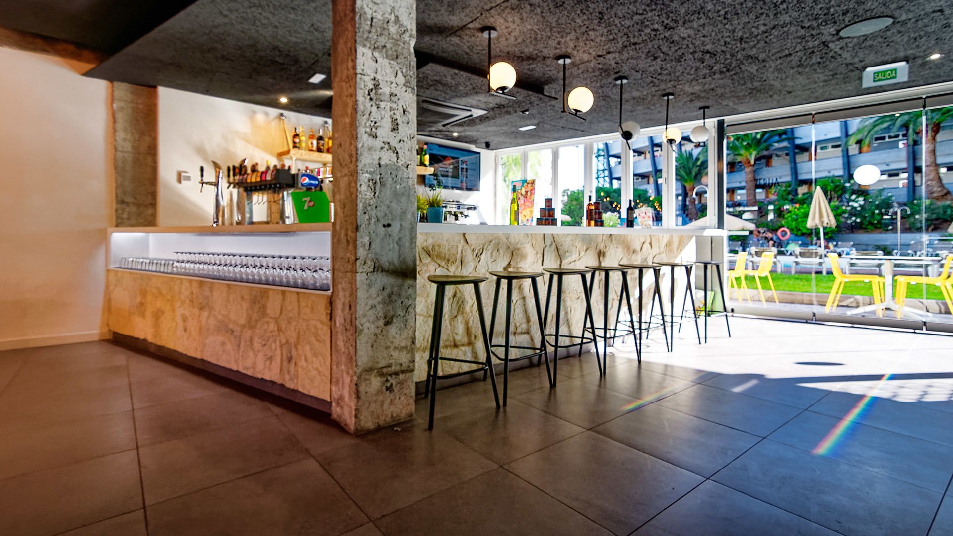 A bar area with stools, a counter with bottles, and a view of the outside.