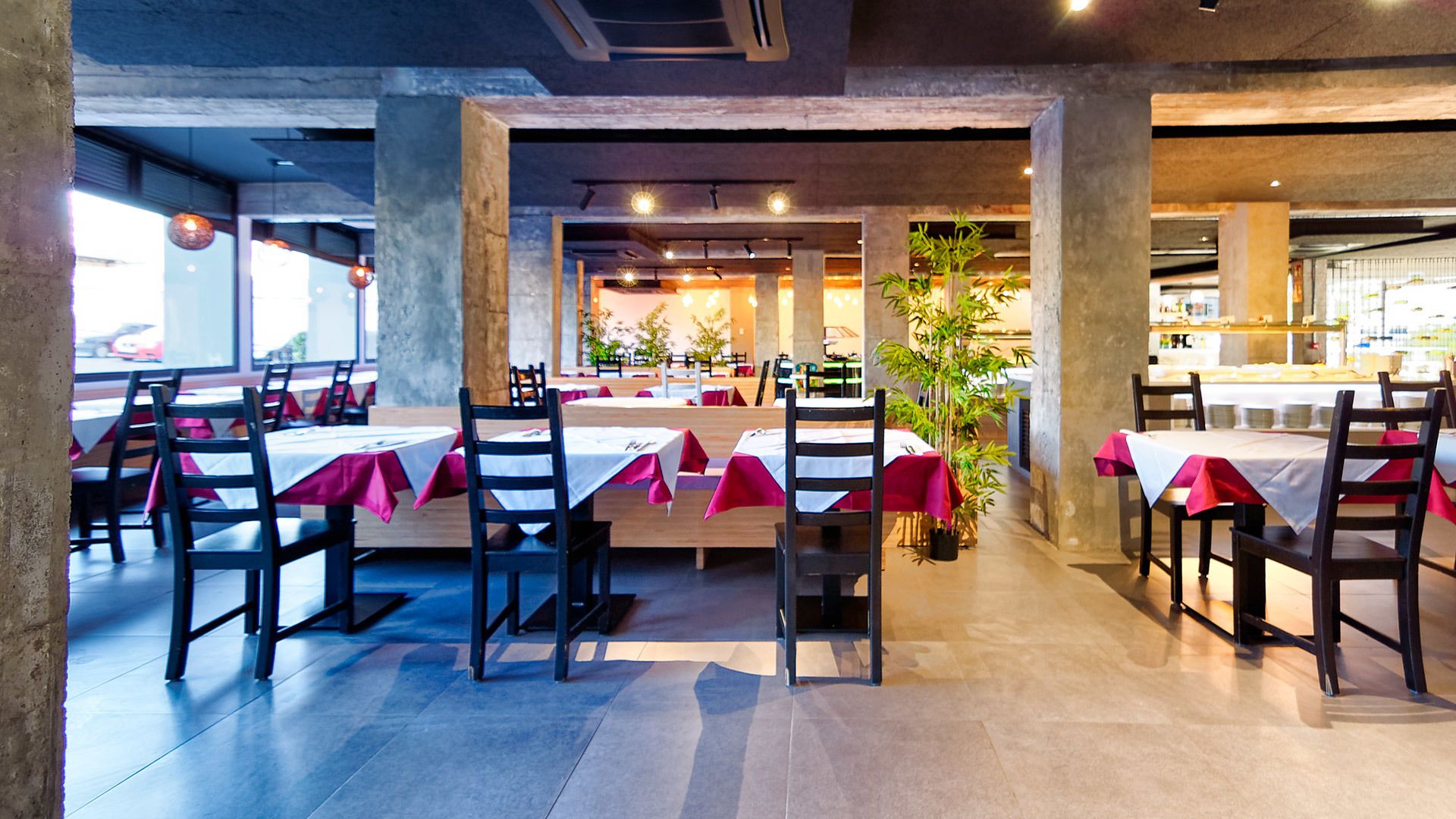 Un restaurant où les tables sont recouvertes de nappes blanches et de serviettes rouges, avec des chaises en bois et des plantes en pot.
