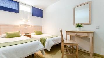 A hotel room with two beds, a desk, a chair, a mirror, and a potted plant.