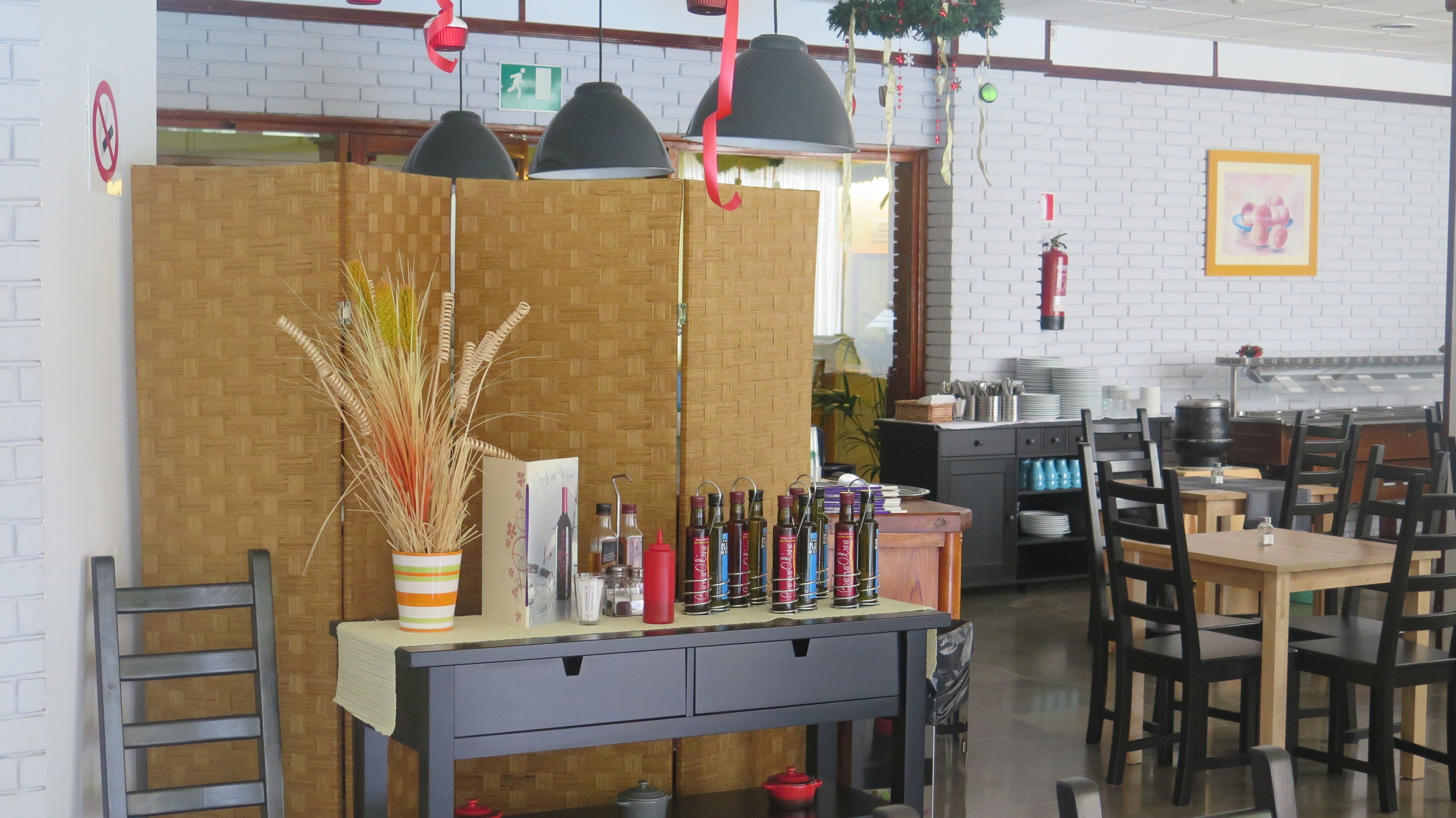 Een restaurantinterieur met een houten scheidingswand, hangende hanglampen en diverse kruidenflesjes op een toonbank.