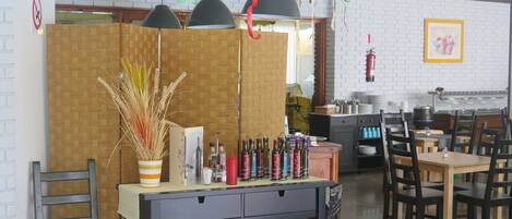 A restaurant interior with a wooden partition, hanging pendant lights, and a variety of condiment bottles on a counter.