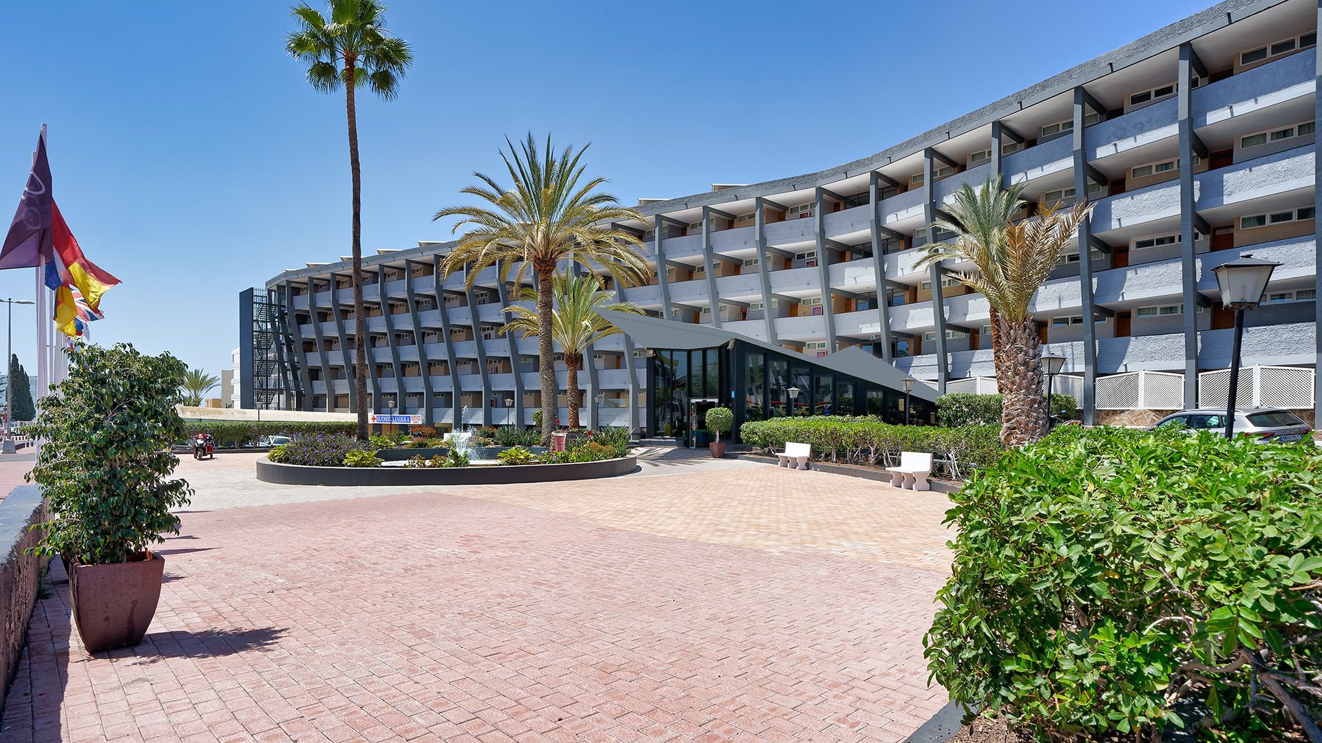 A modern hotel with a central courtyard, palm trees, and a clear blue sky.