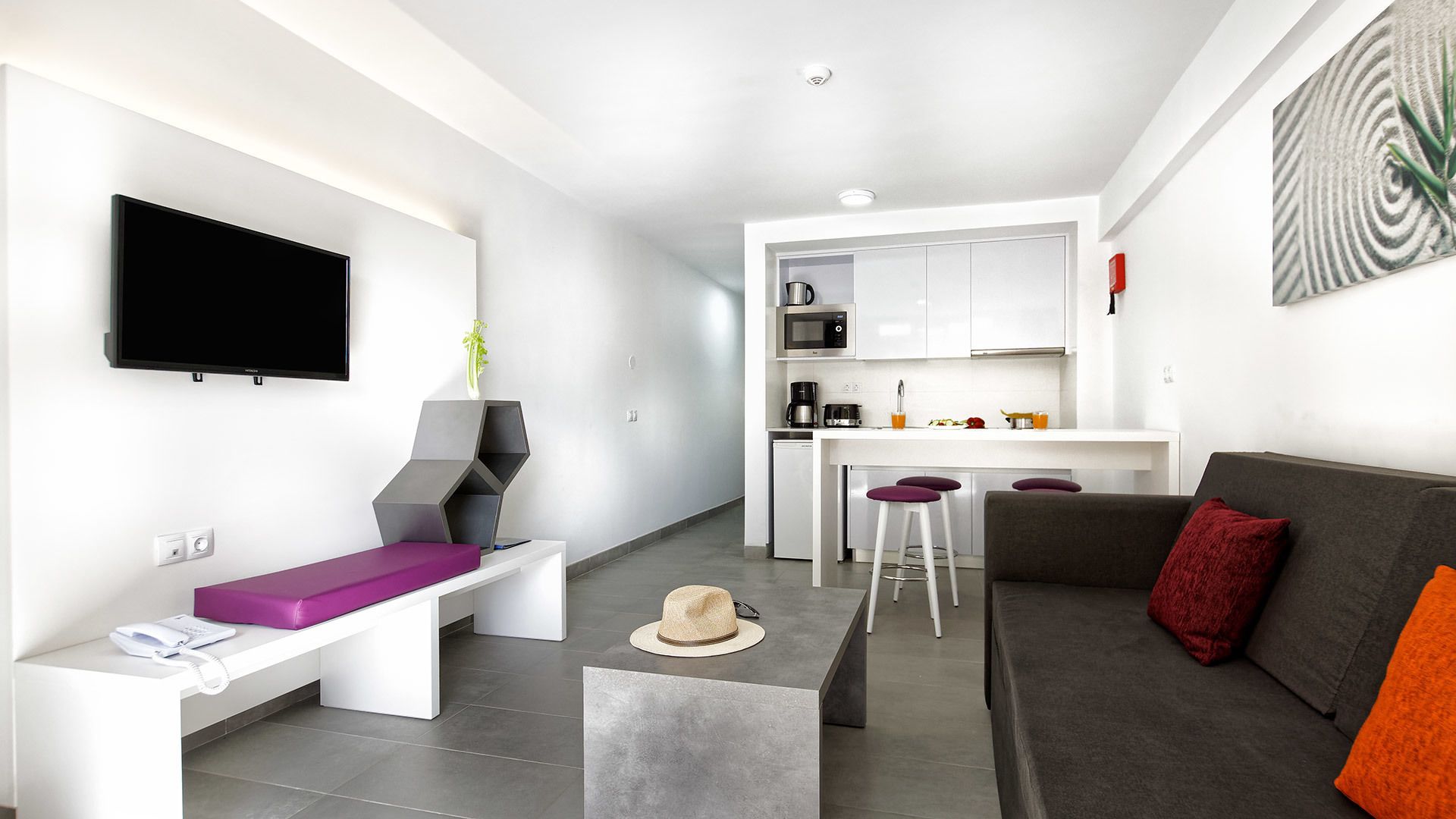 Ein modernes Wohnzimmer mit Flachbildfernseher, einer Bank, einer Couch und einer Küchenzeile.