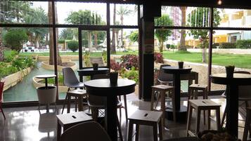 Un restaurante con terraza, ventanas amplias y vistas a un jardín ajardinado.