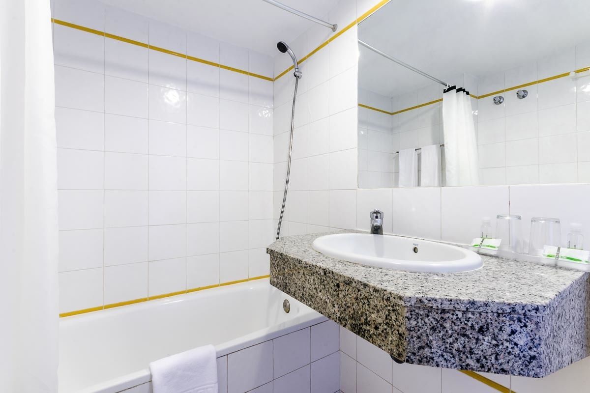 Un baño moderno con azulejos blancos, lavamanos de granito, bañera y un espejo grande.