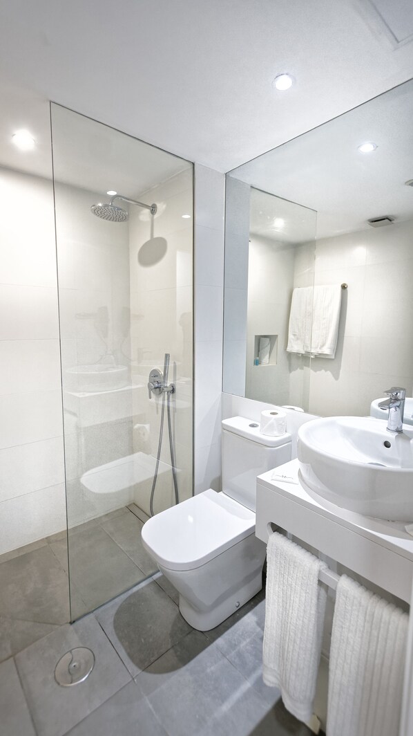 Un baño moderno con cabina de ducha de vidrio, inodoro blanco, lavamanos y espejo.