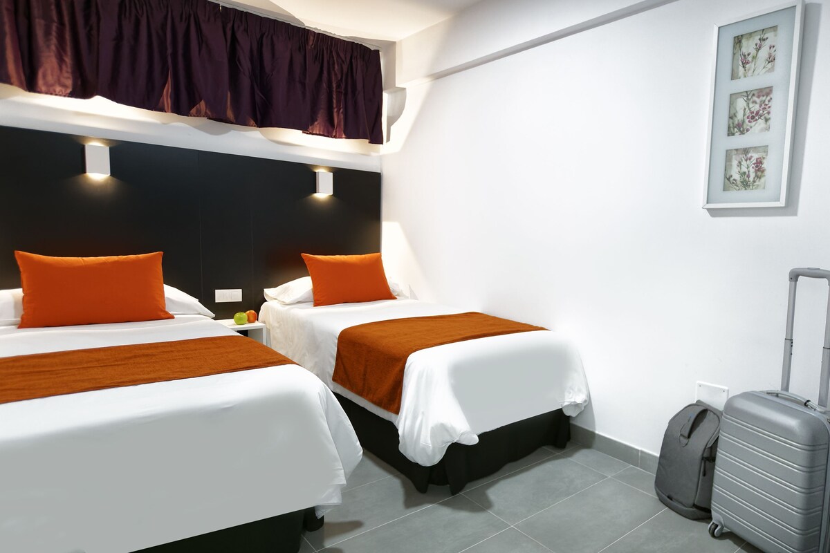 A hotel room with two beds, a suitcase, and a wall-mounted artwork.