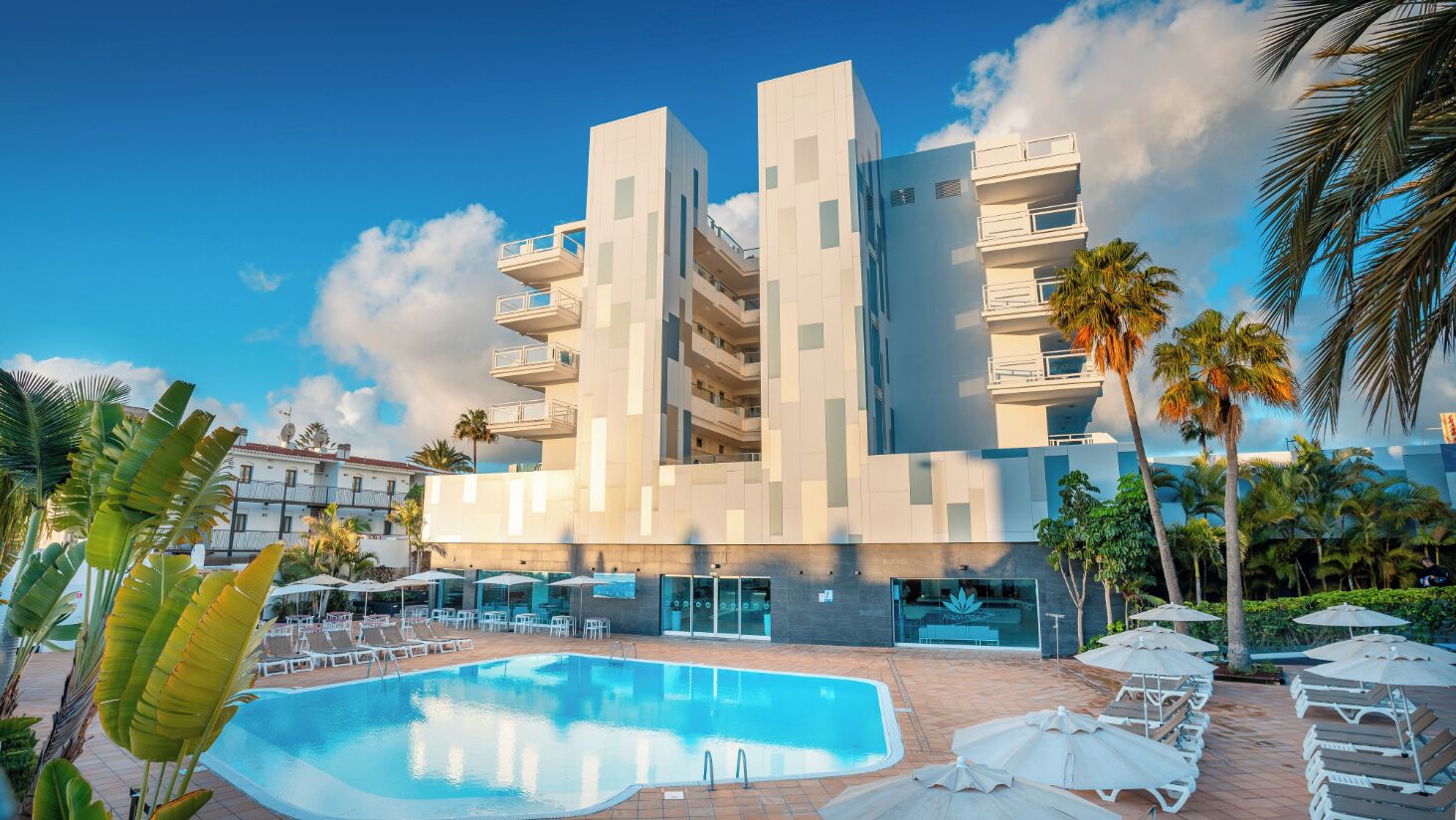 Ein modernes Hotel mit Poolbereich, mehreren Balkonen und Palmen.