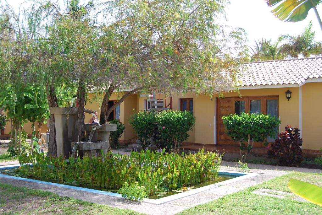 A yellow building with a tiled roof, a small garden with a water feature, and a staircase leading to the entrance.