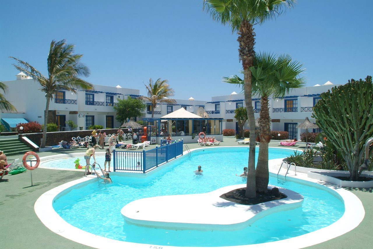 A pool area with multiple swimming pools, palm trees, and a building with blue balconies.