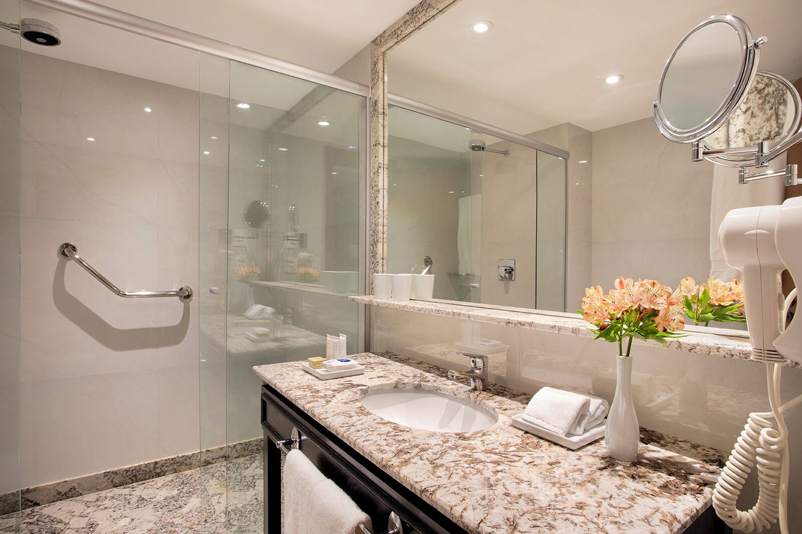 A modern bathroom with a glass-enclosed shower, a marble sink, and a vanity with a mirror and towel rack.