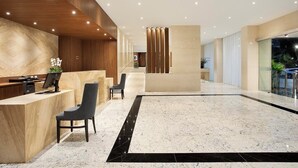 Un área de recepción moderna con piso de mármol, mostrador de madera y una zona de estar con sillas.