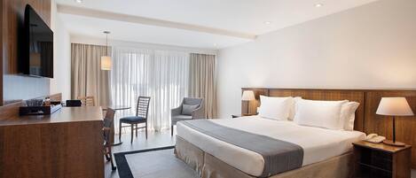 A hotel room with a large bed, a desk, a chair, a TV, and a lamp.