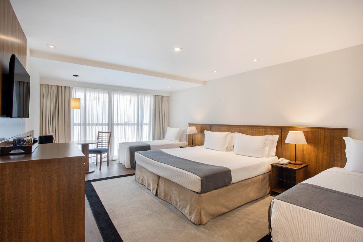 A hotel room with a large bed, a desk, a chair, a TV, and a window with curtains.