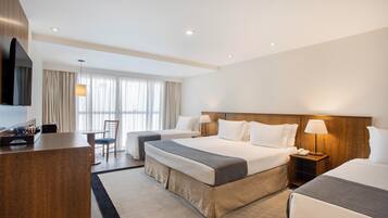 Quarto de hotel com uma cama grande, uma escrivaninha, uma cadeira, uma TV e uma janela com cortinas.