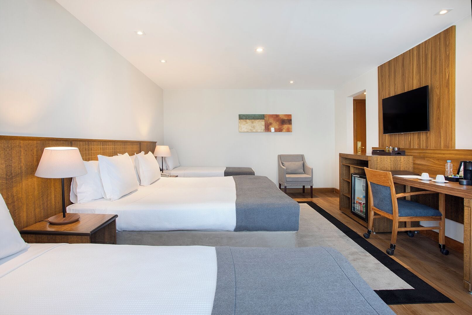 Quarto de hotel com duas camas, uma escrivaninha, uma cadeira, televisão e uma pequena cozinha.