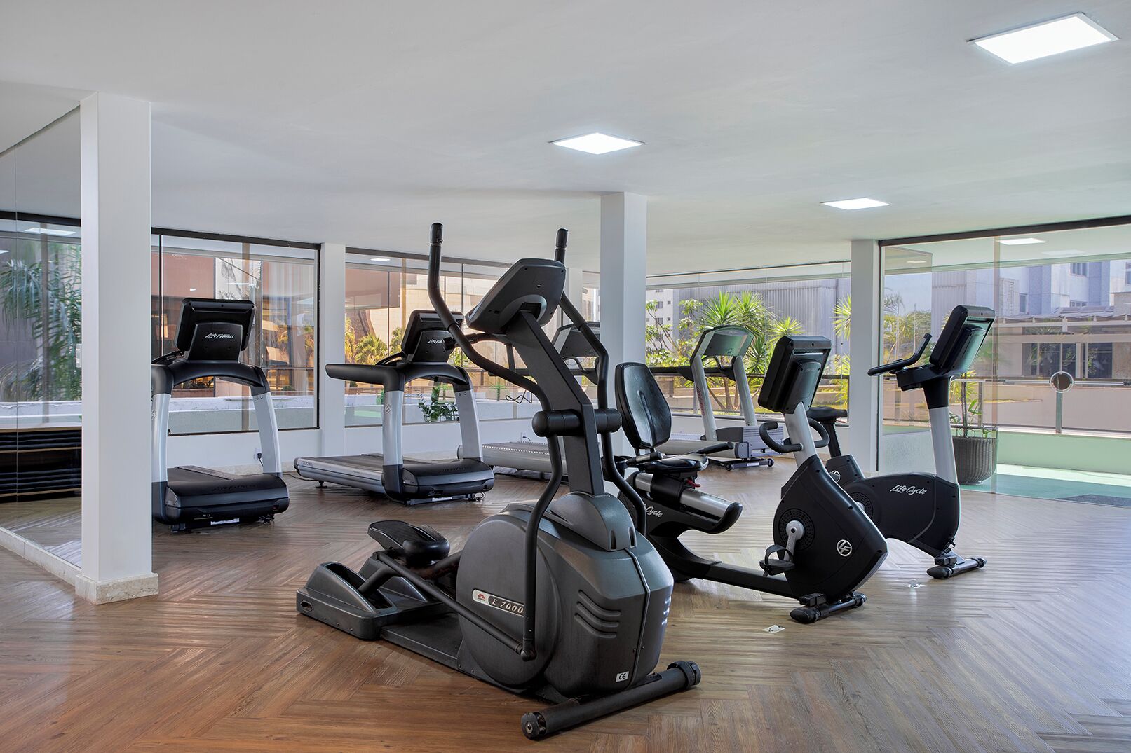 Un gimnasio con cintas de correr, elípticas y bicicletas estáticas, ventanas amplias y piso de madera.