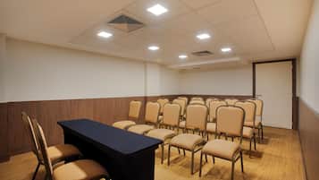 A conference room with a long table and multiple chairs, equipped with ceiling lights and a vent.