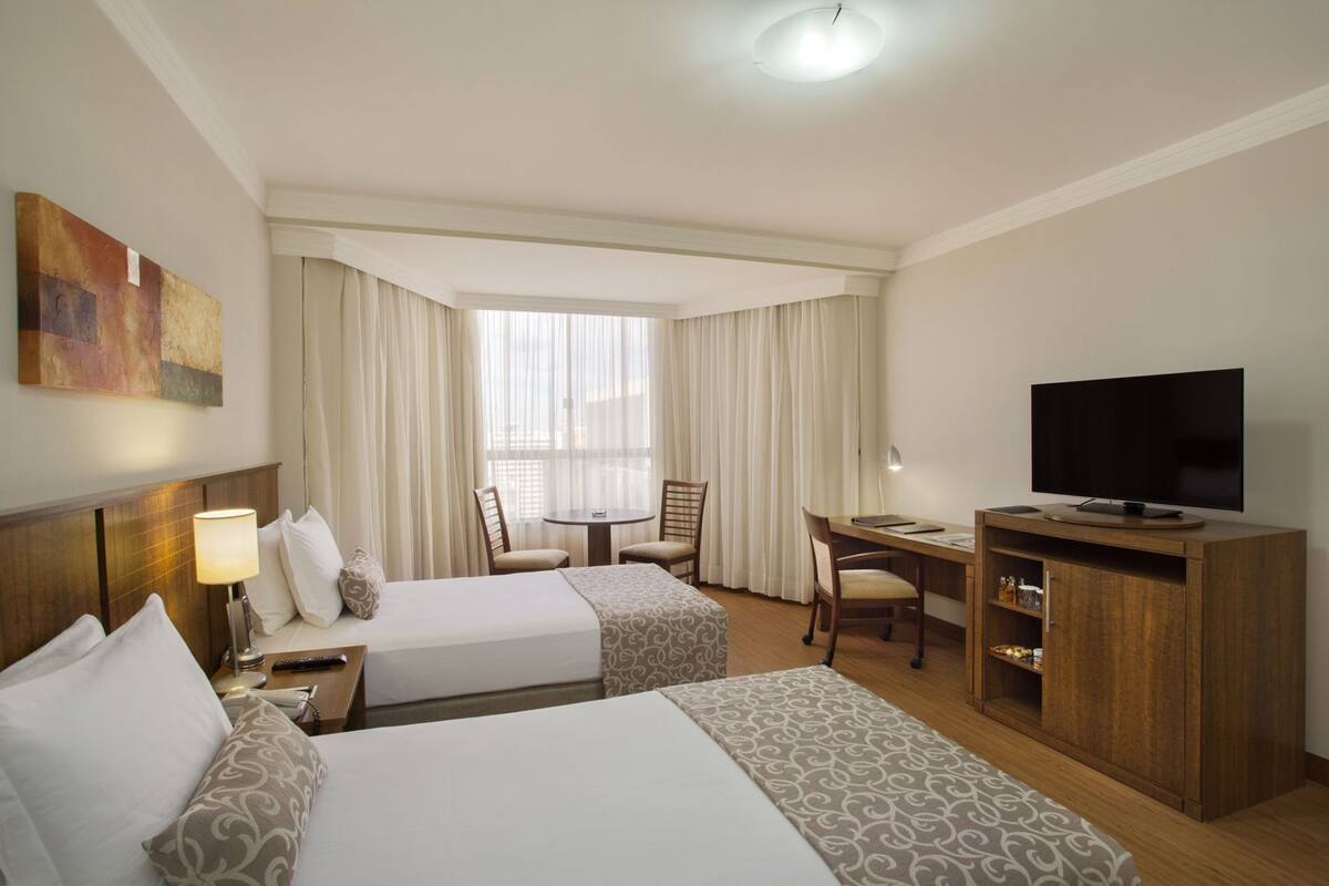 A hotel room with two beds, a desk, a television, and a chair.