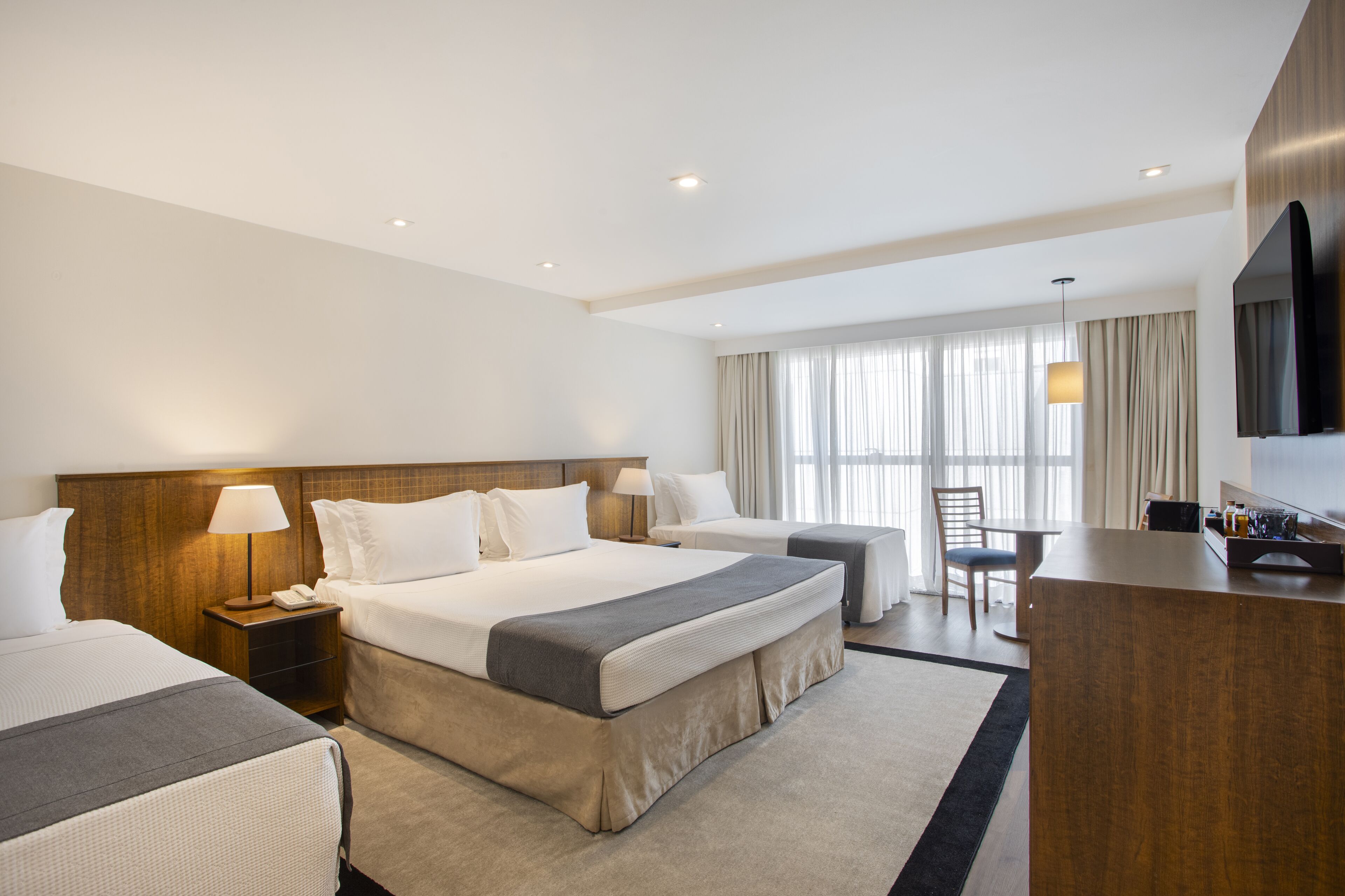 Habitación de hotel con una cama grande, un escritorio, una silla, un televisor y una ventana con cortinas.