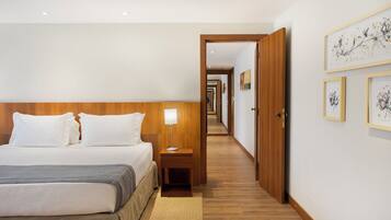 A hotel room with a bed, bedside table, lamp, and a hallway leading to another room.
