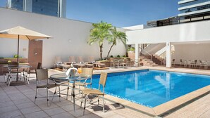 Un área de piscina en la azotea con sillones de descanso, una mesa y una escalera que lleva a un nivel superior.