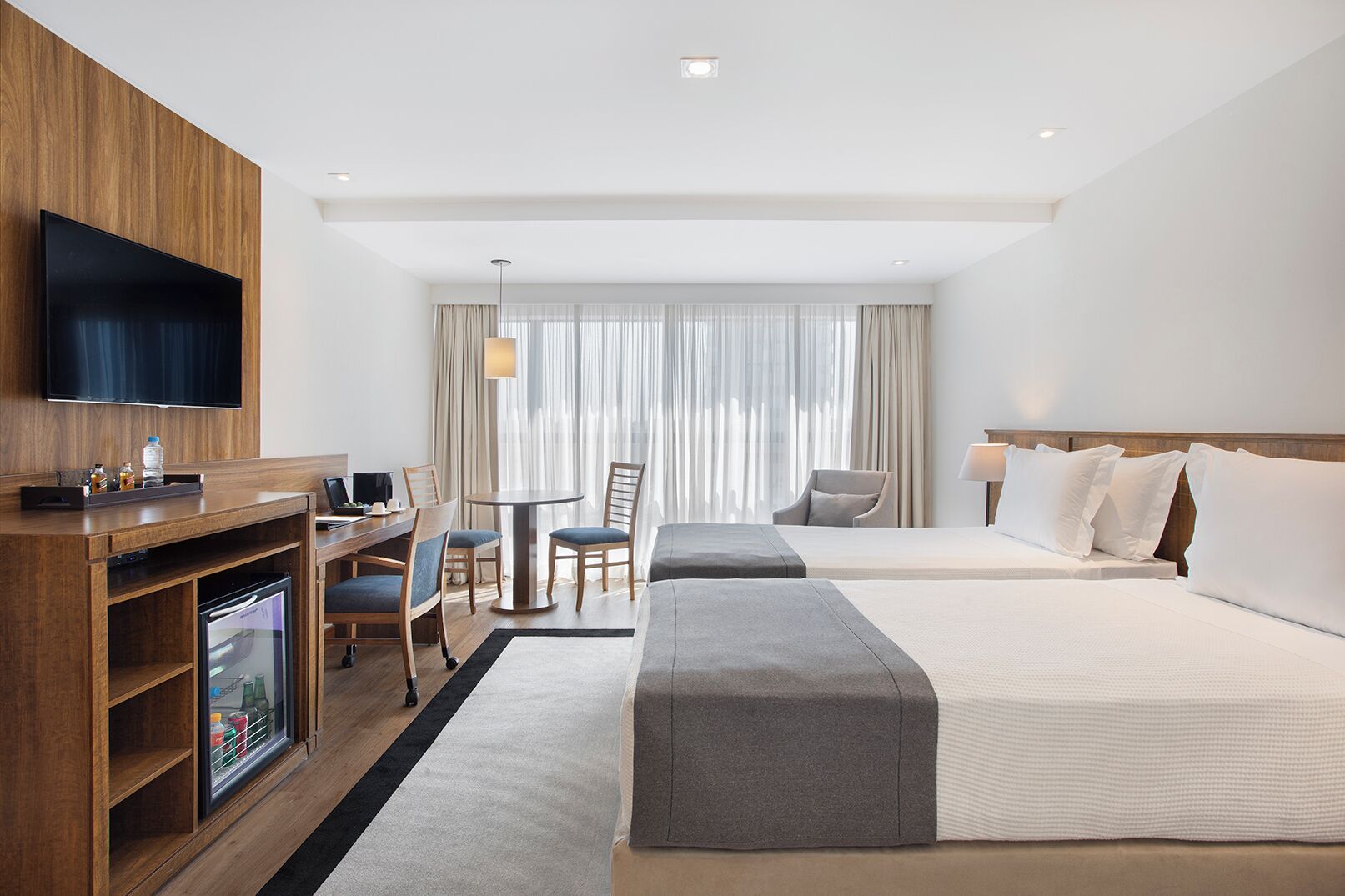 A hotel room with a TV, a desk with a computer, two beds, a chair, and a small refrigerator.