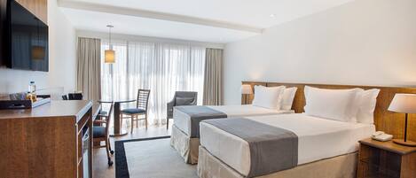 Una habitación de hotel con dos camas, un escritorio, una silla, un televisor y un ventanal con cortinas.