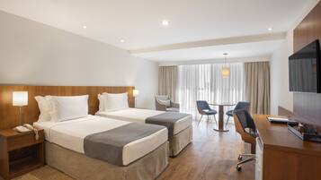 A hotel room with two beds, a desk, a chair, a TV, and a window with curtains.