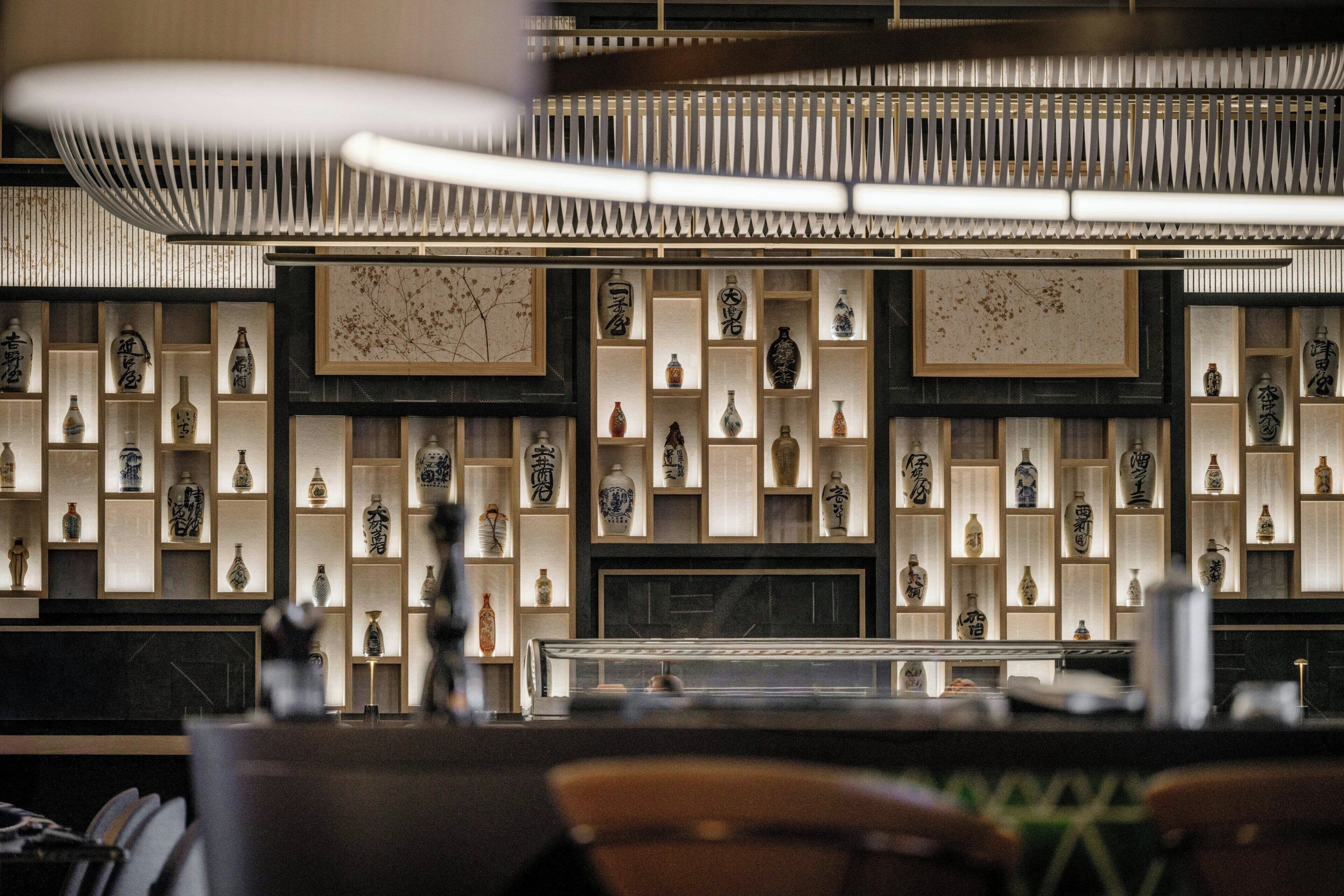 L’intérieur d’un restaurant présente une décoration asiatique traditionnelle, avec une variété de vases en céramique et d’œuvres d’art exposées sur des étagères.