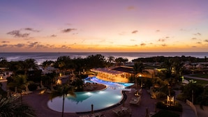 A resort with a pool, lounge chairs, and a view of the ocean at sunset. - The Ritz-Carlton, Aruba (Noord)
