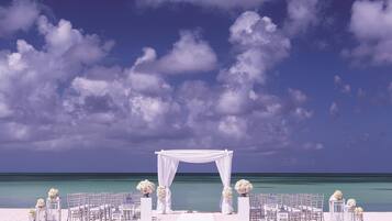 Decoración para una boda en la playa, con un arco blanco y sillas dispuestas para los invitados.