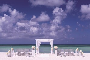 A beach wedding setup with a white arch and chairs arranged for guests.