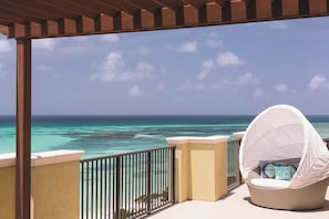 A balcony with a wicker chair and a white canopy, overlooking a turquoise sea.