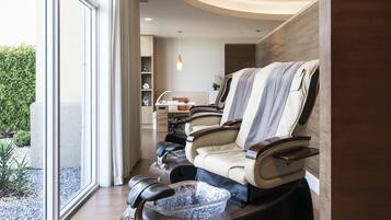 Un moderno salón de spa con un ventanal grande, una silla de masaje y una mesita con un cuenco.
