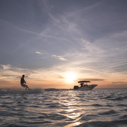 A person wakeboarding on the water with a boat in the background during sunset.