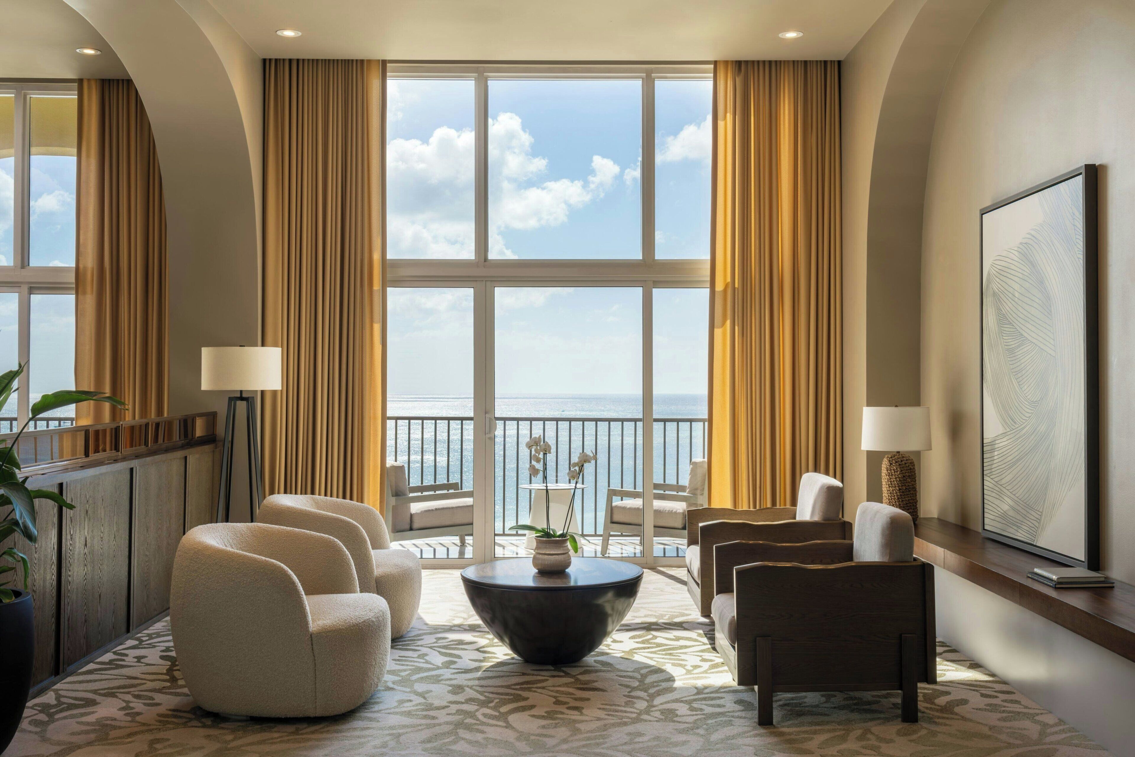 Une chambre d’hôtel dotée d’une grande fenêtre, d’une table basse ronde et de différents sièges.