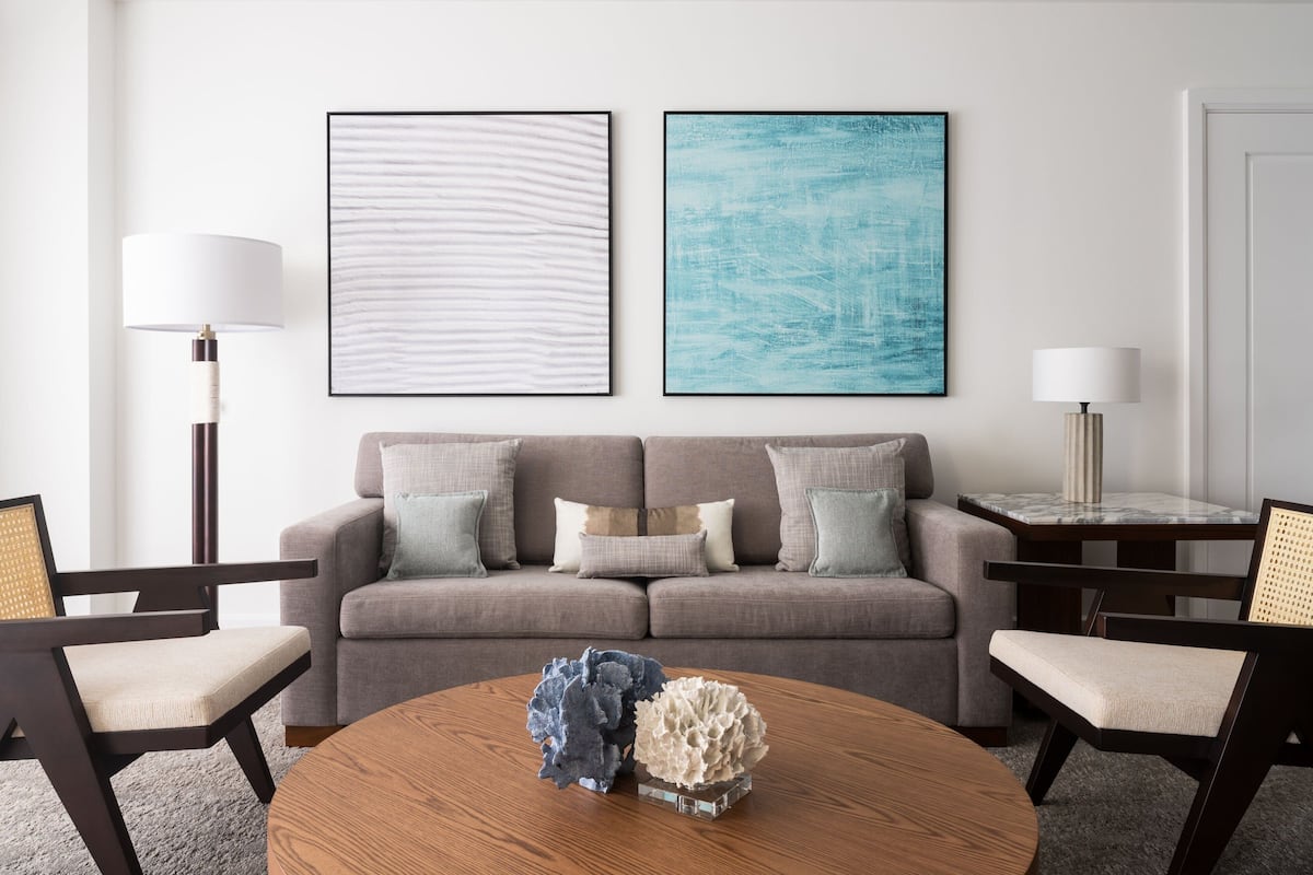 Una sala de estar moderna con un sofá gris, dos obras de arte enmarcadas, una mesa de centro redonda de madera y dos sillones.